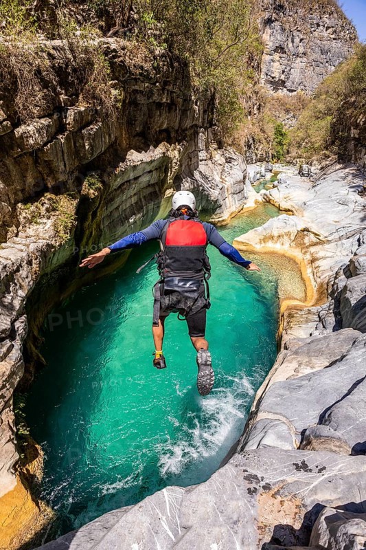 A canyoneer leaps into vibrant turquoise waters surrounded by rugged cliffs in Matacanes, Nuevo Leon, Mexico, enjoying a thrilling day of canyoning and exploration