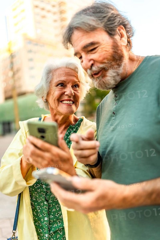 Vertical close-up of a happy senior couple walking using mobile phone in the city
