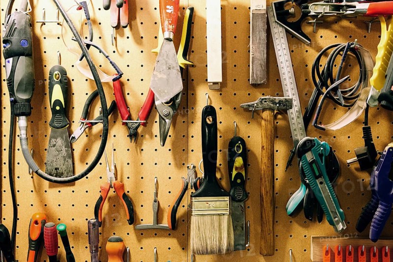 Pegboard displaying assorted luthier tools for crafting bass guitars, including pliers, brushes, files, and more, organized neatly, reflecting craftsmanship and precision