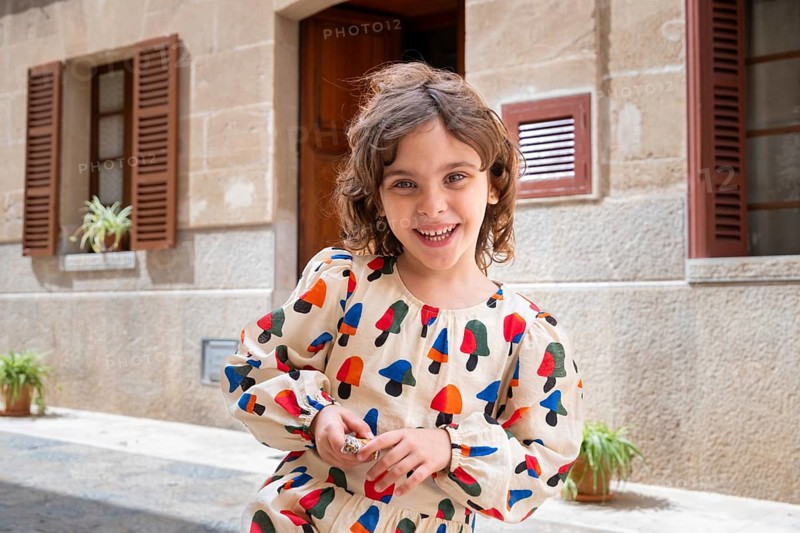 A joyful child, dressed in colorful attire, plays in the sunlit street of a quaint village, expressing happiness and innocence amidst charming rustic surroundings
