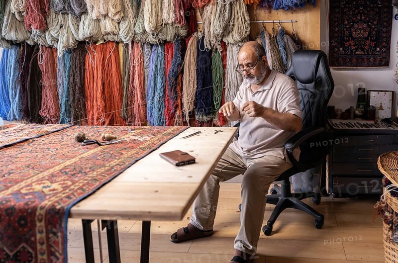 An Iranian master craftsman meticulously restores a carpet in his well-organized workshop in Salzburg, Austria, surrounded by colorful yarns