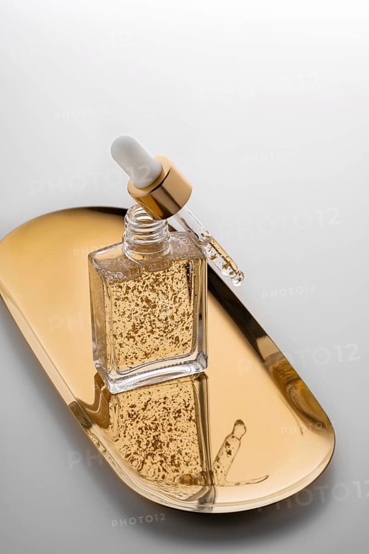A high-end face serum enriched with gold flakes, presented in a stylish glass bottle with a dropper, resting on a golden tray, symbolizing opulence and skincare luxury