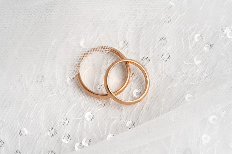 Close-up of two intertwined rose gold wedding rings atop a delicate white lace fabric, symbolizing eternal love and commitment