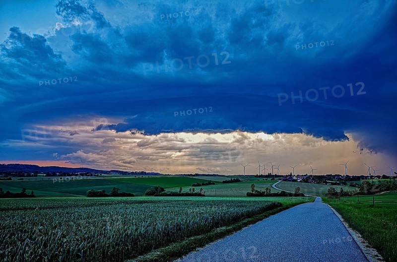 Aufziehendes Gewitter mit imposanter und bedrohlicher Wolkenformation einer Gewitterzelle über einem Dorf mit Windrädern im Hintergrund, Baden-Württemberg, Deutschland