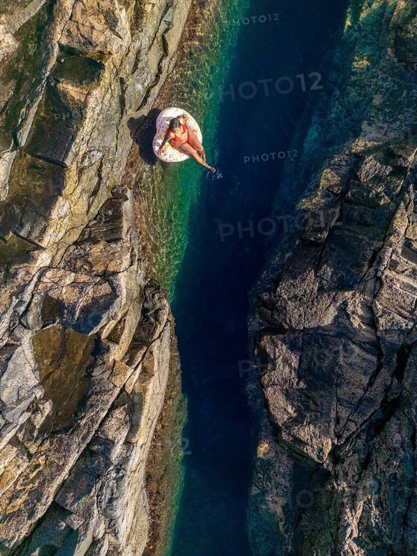 Top view of an unrecognizable woman floating on an inflatable in the clear, waters of a natural pool on the rugged coastlines of Tindaya Beach, Fuerteventura. Capturing the tranquility and untouched beauty of this hidden gem in the Canary Islands