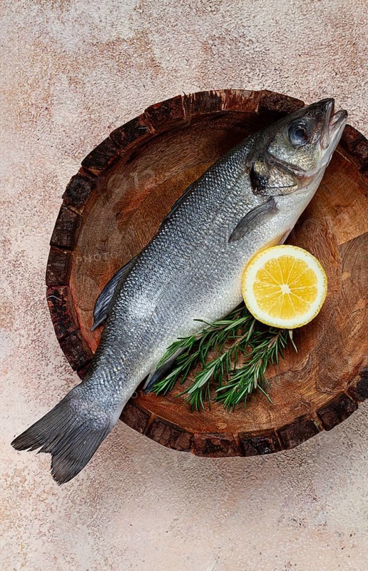Fresh, raw sea bass fish, in a wooden plate, top view, no people.