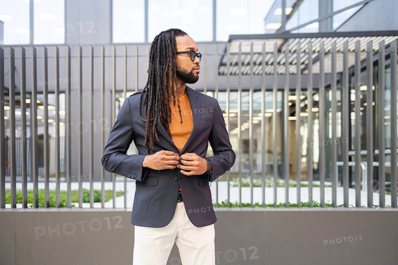 A cuban business man in a dark blazer and sunglasses stands confidently against a contemporary building backdrop, embodying urban sophistication and modern style