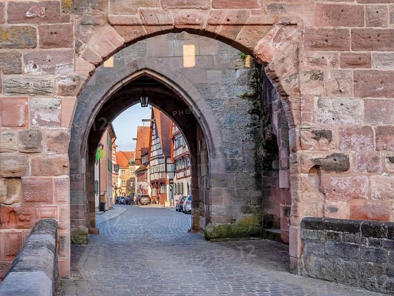 Alley with cobblestones leads through the town gate Oberes Tor, view through the gate to the half-timbered houses of the old town in the evening light, Wolframs-Eschenbach, Middle Franconia, Bavaria, Germany
