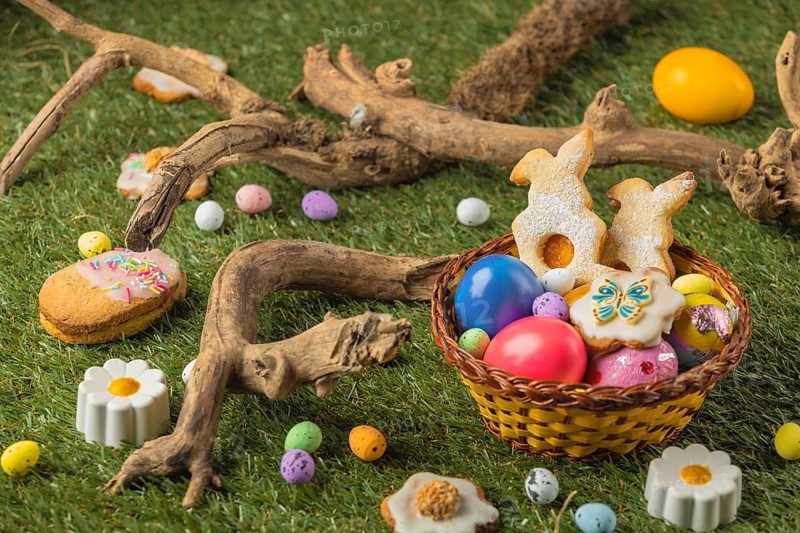 An Easter basket with cookies and eggs in a meadow surrounded by wooden decorations