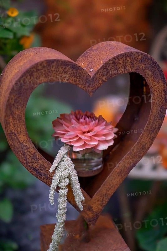 Rusty heart with pink flower in a glass in front of a soft, green backdrop, North Rhine-Westphalia, Germany