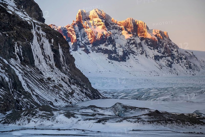 Captivating Icelandic winter scenery with majestic snow-capped mountains in Skaftafell and expansive glaciers illuminated by a delicate sunset, showcasing natural beauty and tranquility