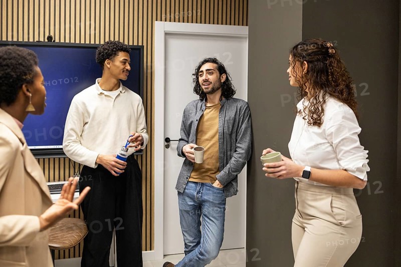 Group of colleagues in a contemporary office setting, engaged in a casual conversation during a coffee break. Modern decor enhances the relaxed atmosphere