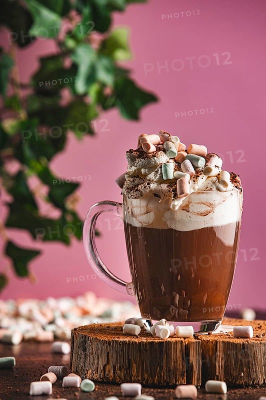 Hot chocolate with whipped cream, cocoa powder and marshmallows on a wooden board, pink background
