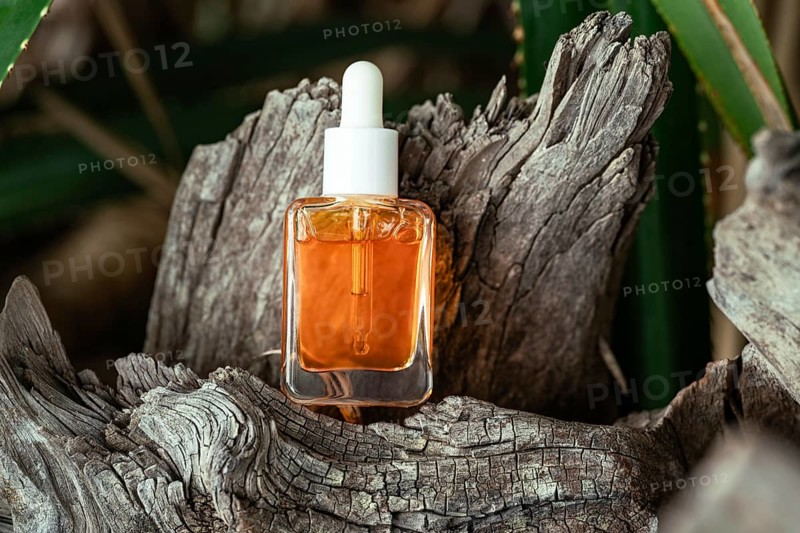 A clear bottle of Vitamin C serum for face care is displayed in a rustic wooden setting surrounded by green foliage, highlighting natural beauty and skincare