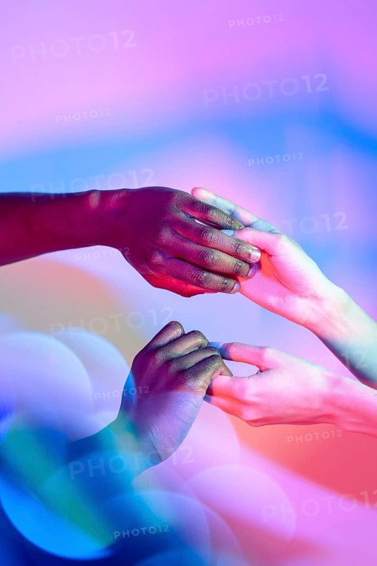 Multiethnic hands gently holding each other with vibrant colored lighting in the background, symbolizing unity and diversity in a harmonious, artistic setting