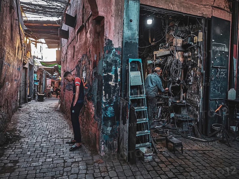 Narrow alley with cobblestones and a workshop, bustling urban atmosphere, small, dark workshop full of cables and metal in the Medina with craftsmen at work, atmospheric lighting, nostalgic atmosphere, Morocco