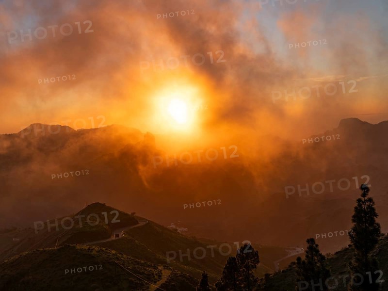 Dramatic sunset lighting up the clouds and mist over the mountains, viewed from Cruz de Tejeda in Gran Canaria, with Roque Nublo in the distance