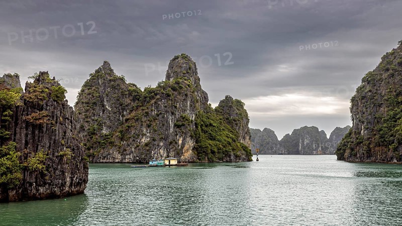Limestone cliffs and small boats on calm waters under a cloudy sky, The landscape and islands of Halong Bay in Vietnam