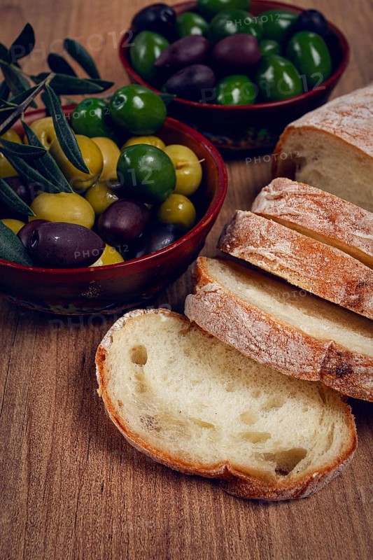 A mixture of olives, varieties of Halkidiki, Verdi giganti and Kalamata, in a bowl, with sliced ciabata bread, top view, no people