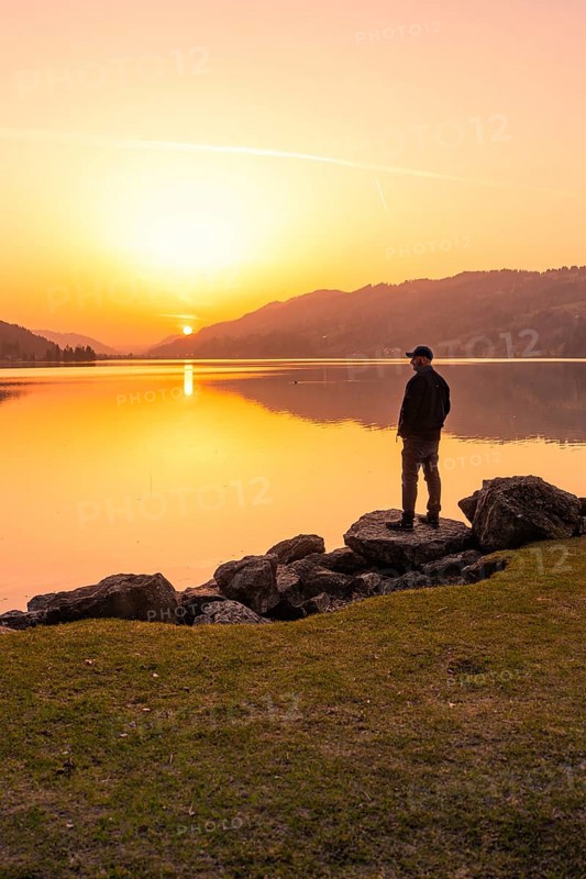 Lonely person standing at the lakeside and watching the sunset, Großer Alpsee, Immenstadt im Allgäu, Bavaria, Germany