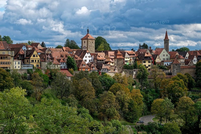 Walls and buildings of the old town of Rothenburg ob der Tauber above the autumnal colourful forest of the hillside above the Tauber valley. Rothenburg, Bavaria, Germany