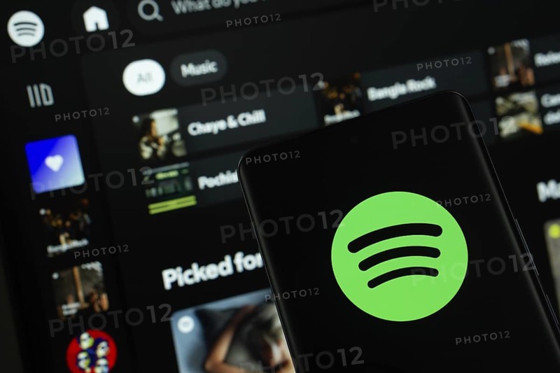 Dhaka, Bangladesh - 18 March 2025: The logo of the spotify is displayed on a smartphone screen, and the website spotify is visible on a computer screen in the background