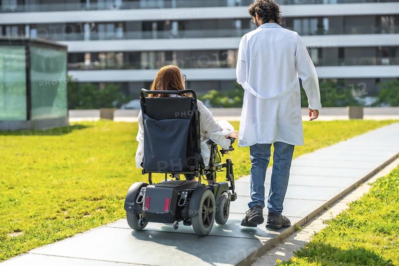 Doctor assisting a patient in an electric wheelchair, strolling through a sunny hospital garden, promoting recovery and well being