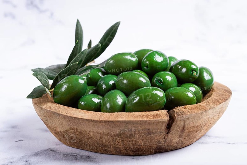 Halkidiki olives, classic Greek green olives, in a wooden bowl, on a marble table, no people