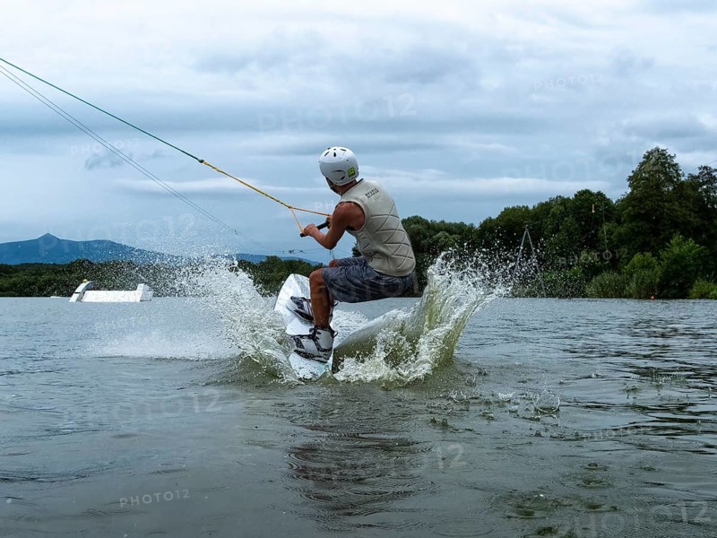 Young man jumping with wakeboard into the lake, water sports, water skiing in wakepark, Stráž pod Ralskem, Czech Republic