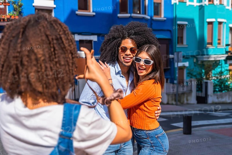 Young woman taking pictures of her two best friends embracing, visiting a colorful city in a sunny day