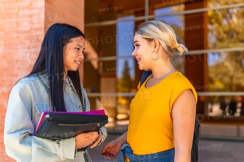 Two multi-ethnic female cauacsian and chinese students discussing outside the university entrance