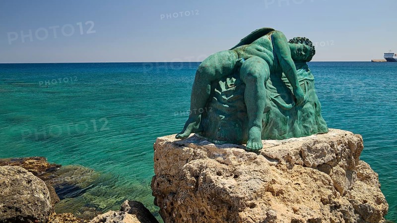 Bronze sculpture, sleeping Eros, sculpture on a rock by the sea with blue water, harbour area, Rhodes Town, Rhodes, Dodecanese, Greek Islands, Greece
