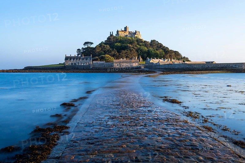 View of St Michaels Mount, in front of it the dam or path, slightly washed over by the tide. Evening, golden hour. St Michael's Mount, Marazion, Cornwall, England, Great Britain