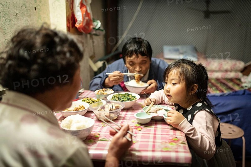 Gao Jian Min (67), Lin Shu Xiang (56) and Gao Xin Rui (5) having dinner, the grandmother bought Nanjing Salt Duck and grilled duck to supplement the dinner, Diao Yu Tai District, Nanjing, China