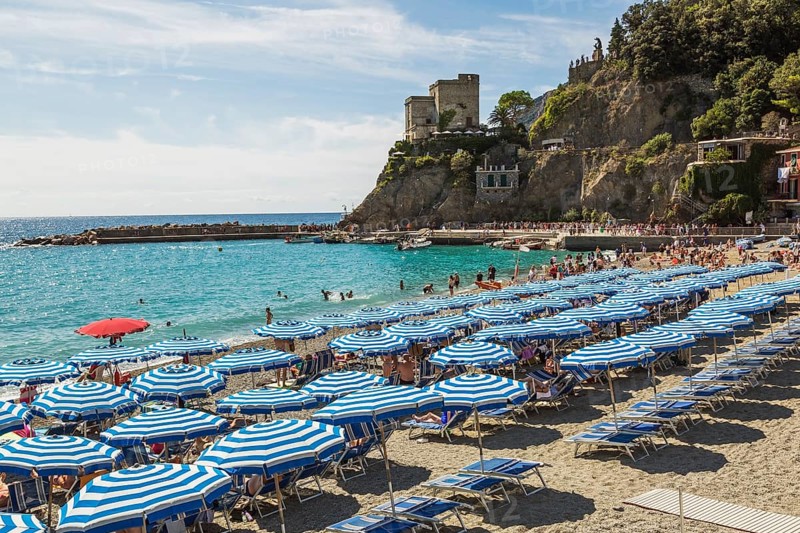 Beach with bathers, tourists and blue parasols in late summer, Monterosso village, Cinque Terre, La Spezia province, Italy