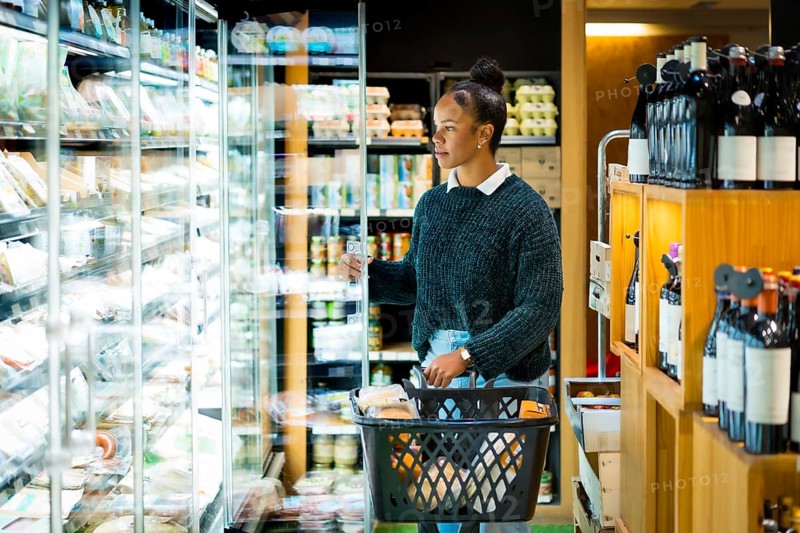 Young woman shopping for groceries, opening refrigerator and choosing fresh food in grocery store