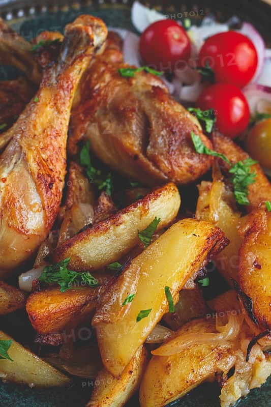 Fried chicken legs with potato slices, on a plate, baked in the oven, with spices, homemade, no people