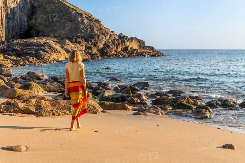 A woman on a sandy beach in Nanjizal Bay. Evening, golden hour. St Just, Penzance, Cornwall, England, Great Britain