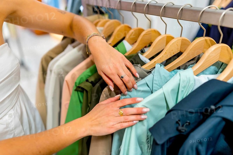 Woman browsing through clothes on hangers in a store, selecting stylish apparel while enjoying a shopping experience in a boutique