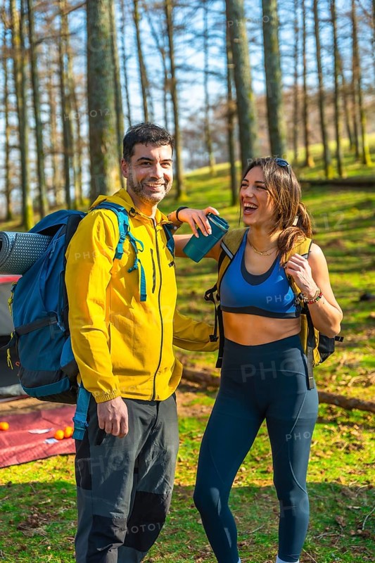 Hikers smiling and enjoying their camping adventure in the serene woods, surrounded by lush trees and the beauty of nature