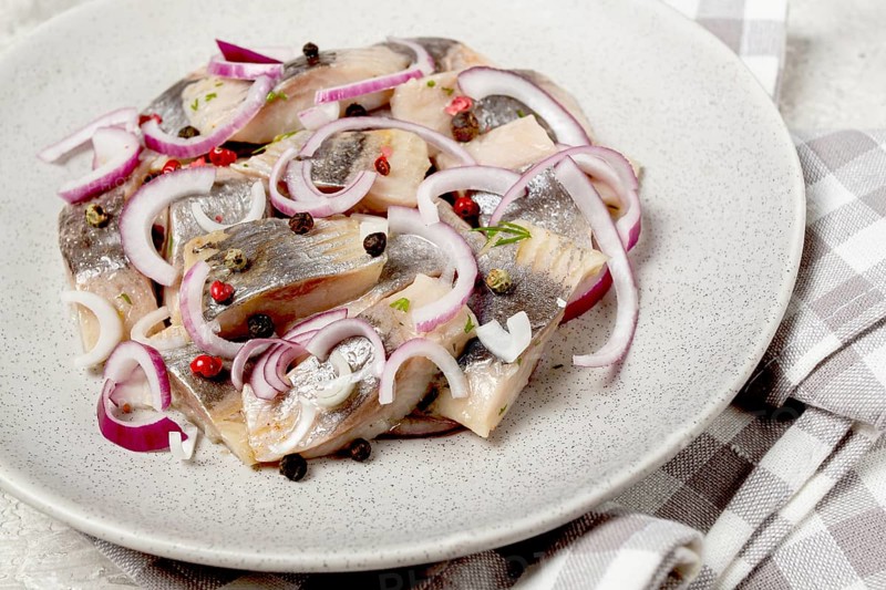 Salted herring, with spices and red onion, sliced fillet, on a plate, top view