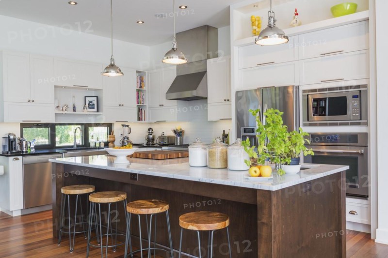 Kitchen area with white cabinets, marble top wooden island with painted black steel and exotic wood barstools, black granite countertops inside a luxurious modern cube style house, Quebec, Canada