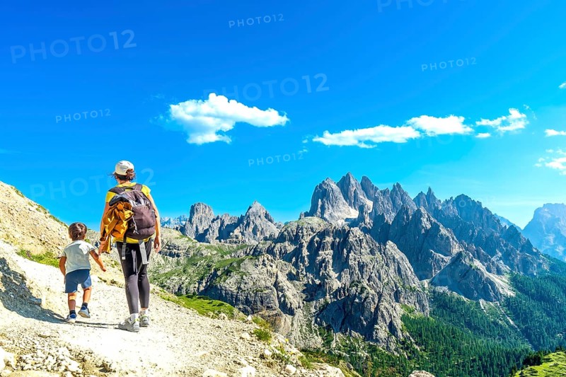 Mother and son walking on a mountain trail in the dolomites, enjoying the breathtaking view of the tre cime di lavaredo on a sunny summer day