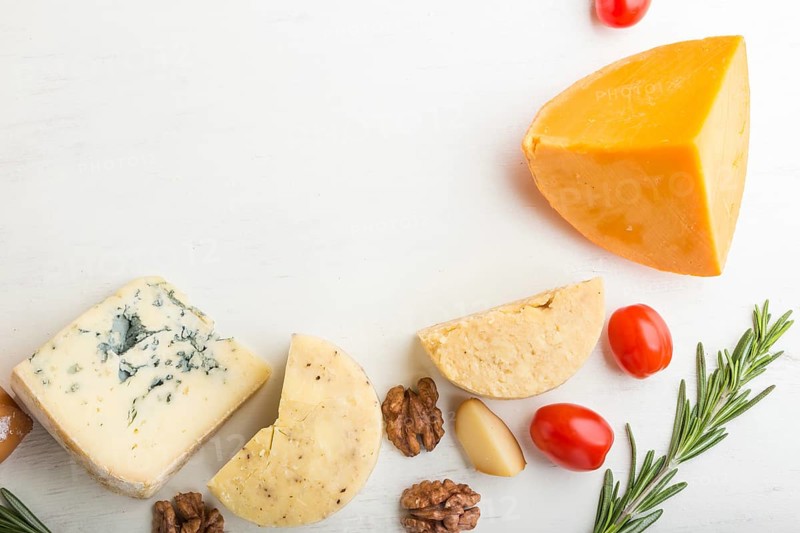 Set of different types of cheese with rosemary and tomatoes on a white wooden background. Top view, flat lay, copy space