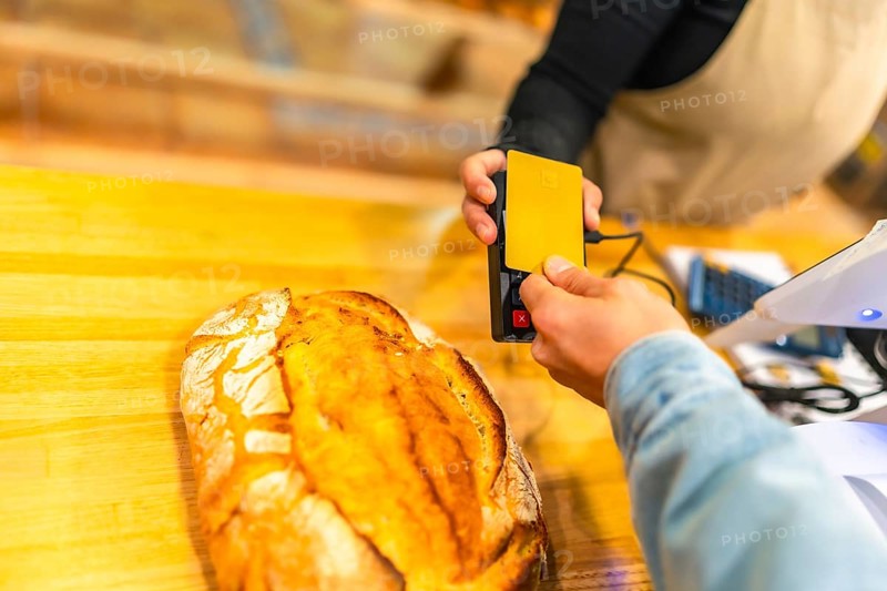 Close-up of the hands of a male client using credit card to pay in a bakery