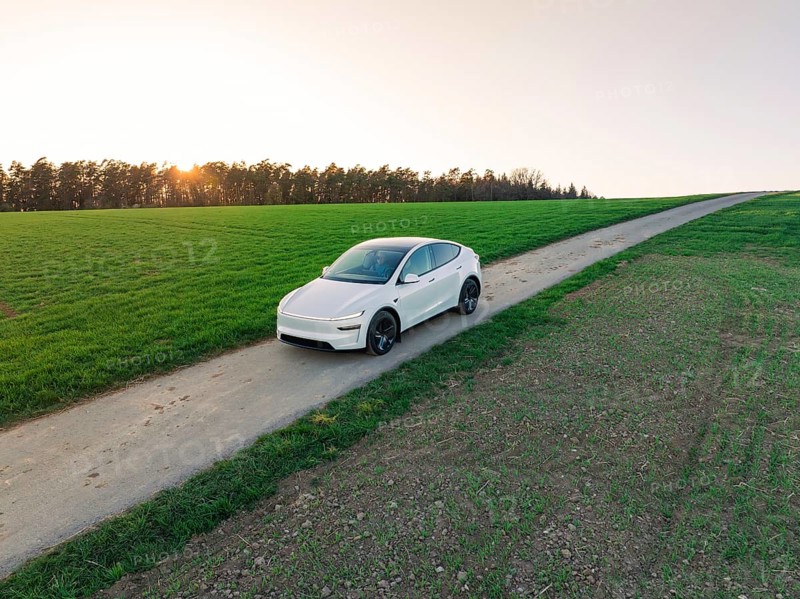 An electric vehicle drives along a remote country road, with sweeping views over fields and a golden sunset, Tesla, New Model Y, Black Forest, Germany