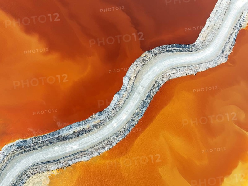 Track crossing a waste pond in the mineral-rich area of the Rio Tinto mines. The colour is caused by oxidised iron minerals. Aerial view. Drone shot. Huelva province, Andalusia, Spain