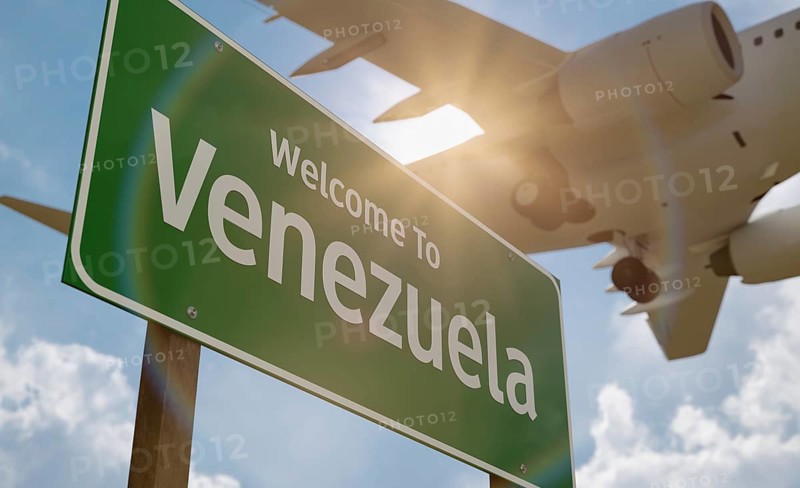 Welcome to Venezuela green road sign with low flying airplane just above with landing gear down
