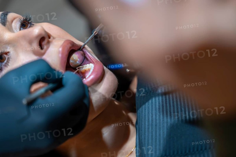 Dentist wearing black gloves using dental mirror and probe examining patient's teeth during consultation in dental clinic