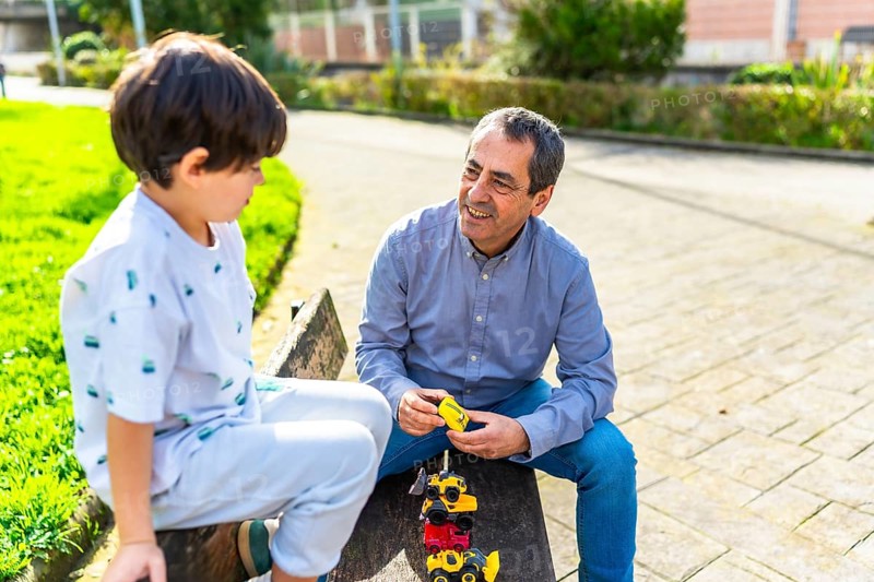 Grandfather and grandson enjoying quality time together, playing with toy trucks in a sunny park, strengthening their bond through play